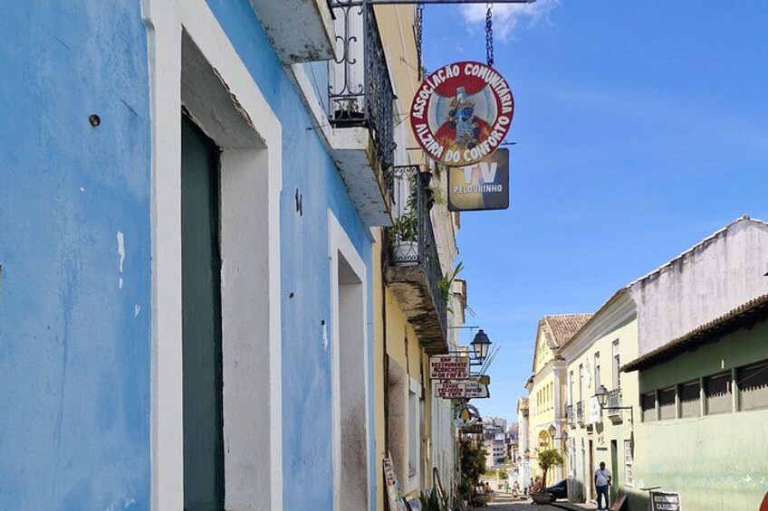 Una stretta via con edifici dipinti di blu e bianco, un cartello per una televisione e un cielo azzurro limpido. 2