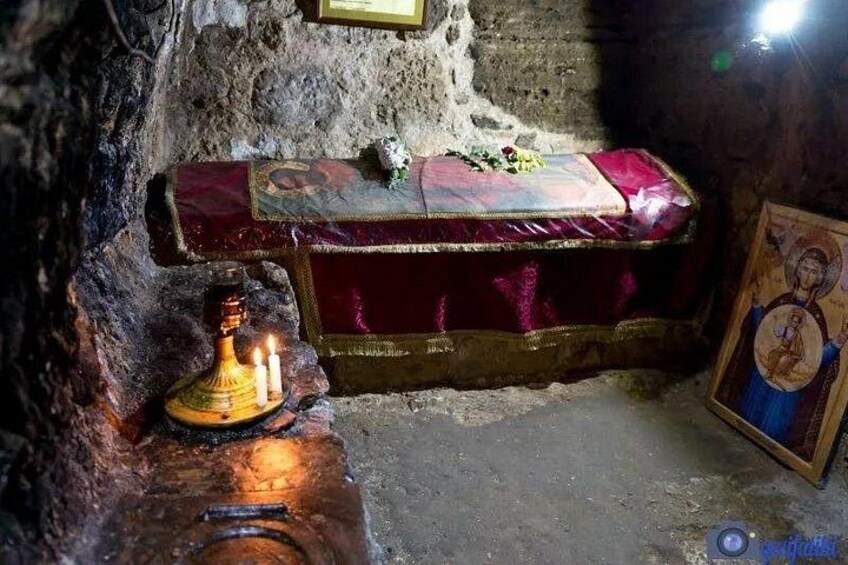 A shrine with a red cloth-covered bench, a lit candle, and a religious icon. 5