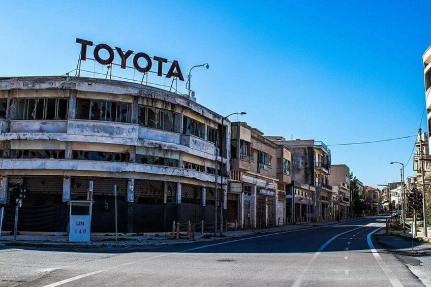 A multi-story building with the word 'TOYOTA' on the top, a street in the foreground, and other buildings in the background. 2