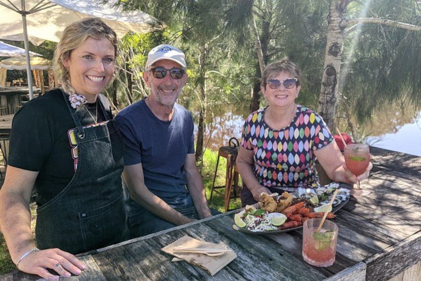 Three people sitting at a wooden table outdoors with food and drinks. 4