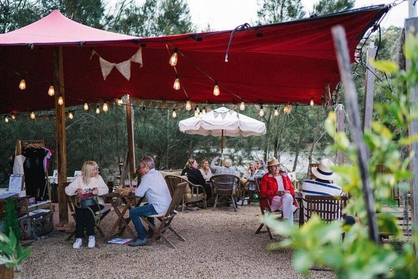 Un encuentro al aire libre con personas sentadas en mesas bajo una toldería roja, rodeado de árboles. 3