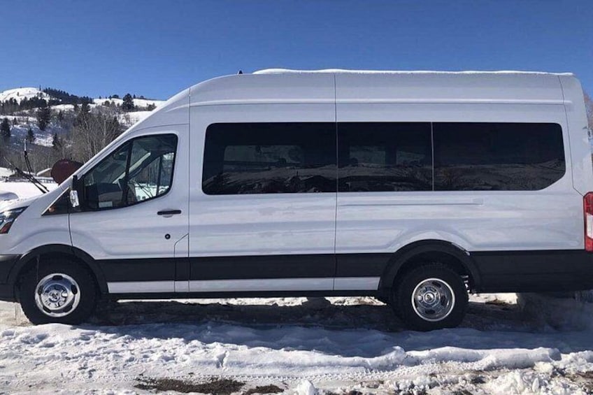 A white van parked on a snowy surface with a clear blue sky and a mountainous background. 2