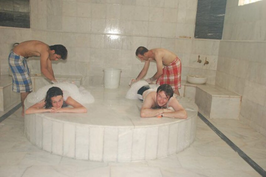 Een groep mensen in een jacuzzi met een marmeren vloer en betegelde muren. 1