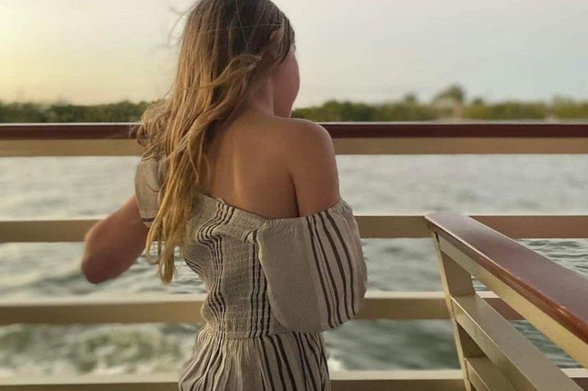 A person in a striped off-shoulder dress standing on a boat deck, looking out at the water. 4