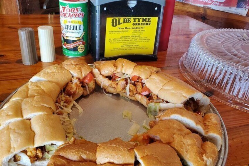 A large sandwich with various fillings, a can of Tony's Creole, a menu board, and a cake on a table. 5