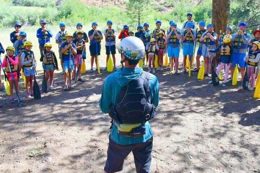 A group of people in a forested area, some wearing life jackets and paddles, likely preparing for a kayaking activity. 5