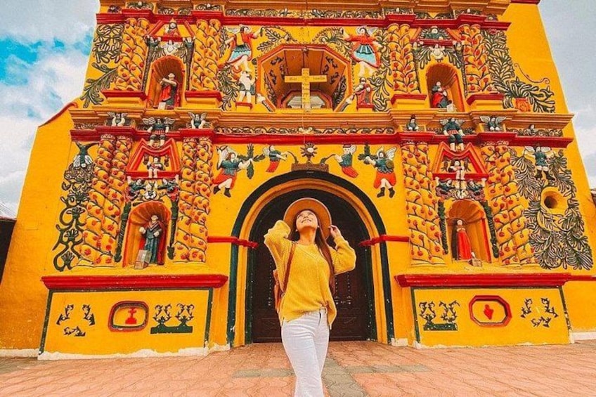 A person standing in front of a brightly painted church with a cross, detailed artwork, and a large archway. 1