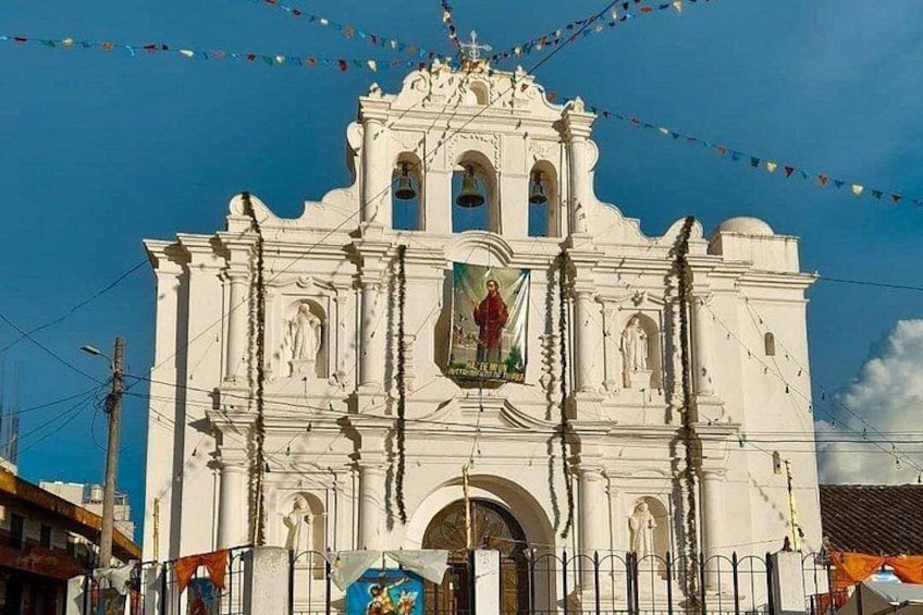 A white church with a bell tower, a large mural, and colorful flags. 2
