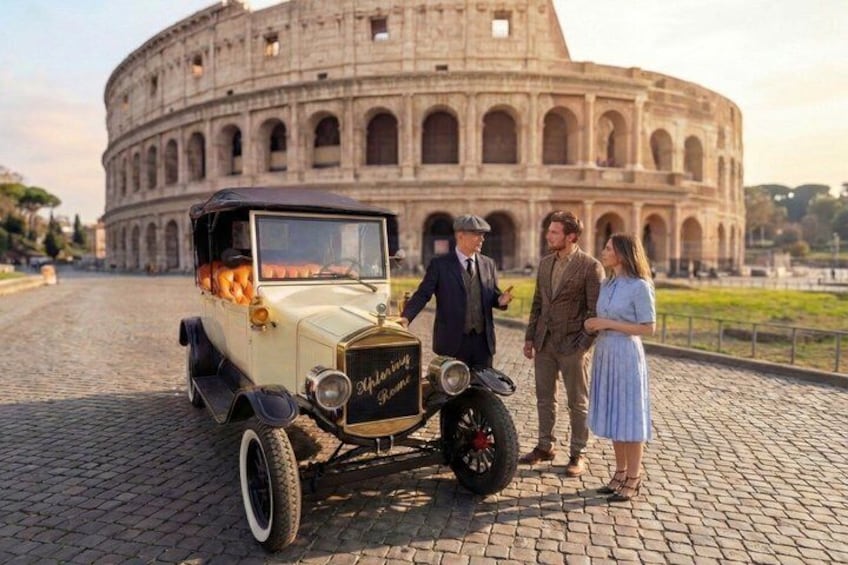 A vintage car parked in front of the Colosseum with three people standing nearby. 5