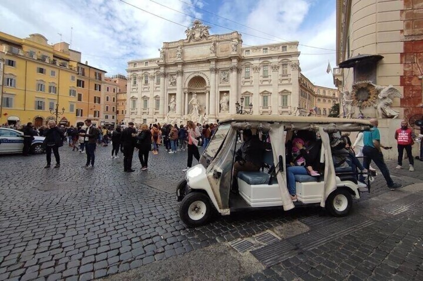 A white golf cart with passengers in front of a historic building. 3