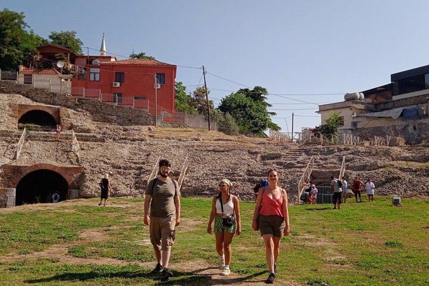 A group of people walking on a grassy path with a historical site in the background, including a red building and a stone structure. 4