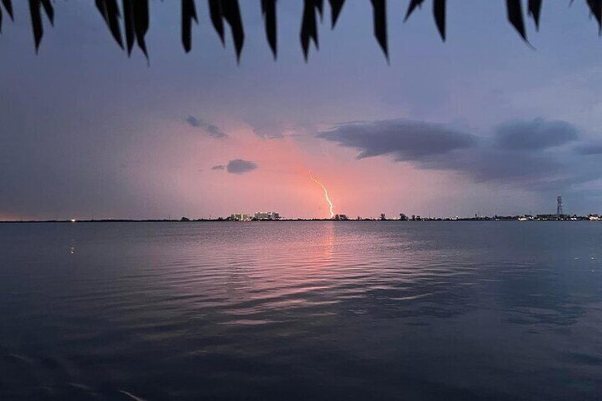A sunset over a calm body of water with a lightning strike in the distance. 4