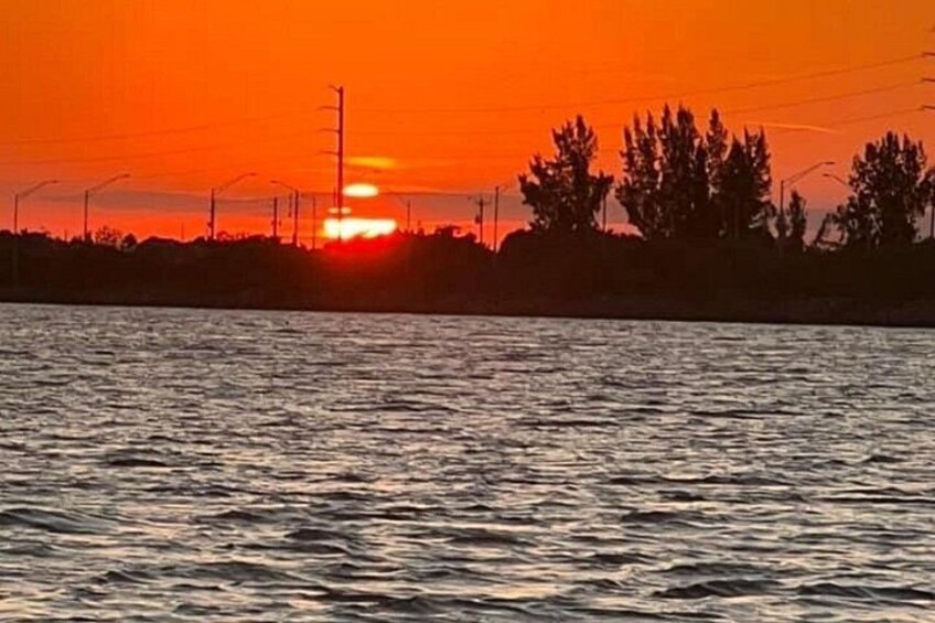 A sunset over a body of water with silhouettes of trees and power lines. 4