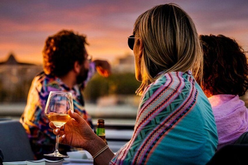 Des personnes sont assises à une table à l’extérieur, au moment du coucher du soleil, et tiennent des verres de vin. 2