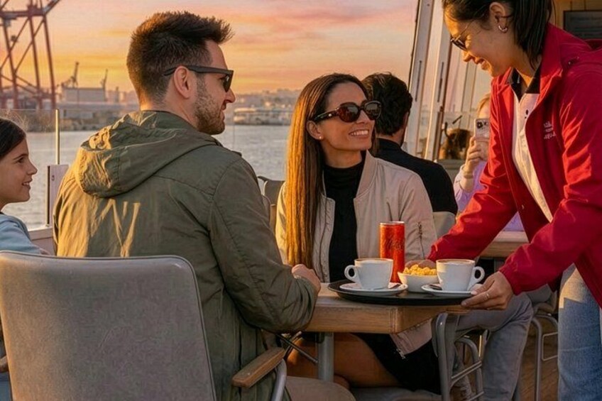 Un groupe de personnes est assis autour d’une table sur un bateau, avec un coucher de soleil en arrière-plan. 3