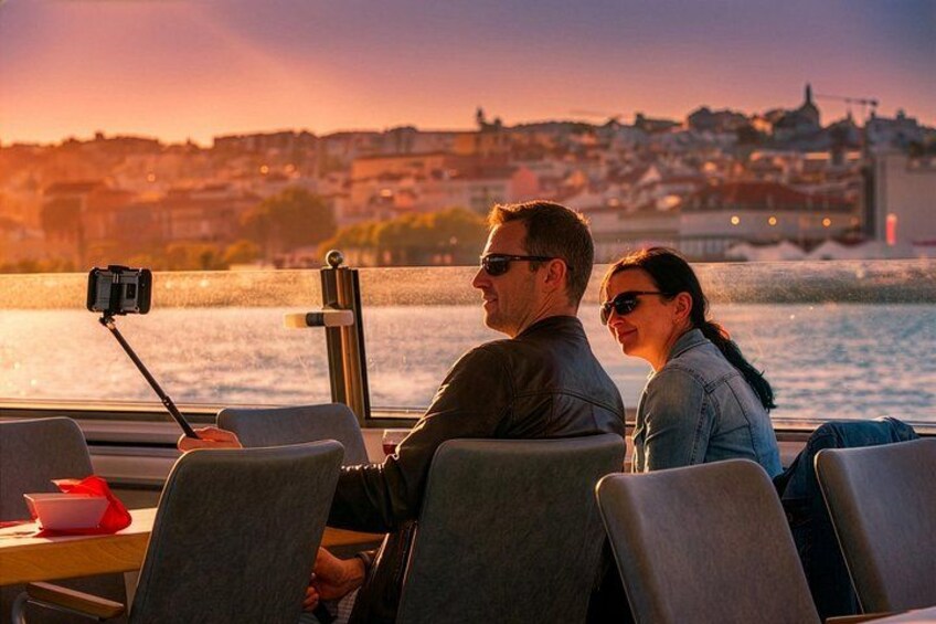 Deux personnes dans un bateau, tenant un bâton à selfie, avec une vue sur la ville en arrière-plan et un coucher de soleil. 4