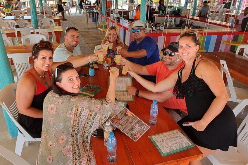 A group of people sitting at a wooden table in a restaurant with white chairs, a menu, and a bottle of water. 4