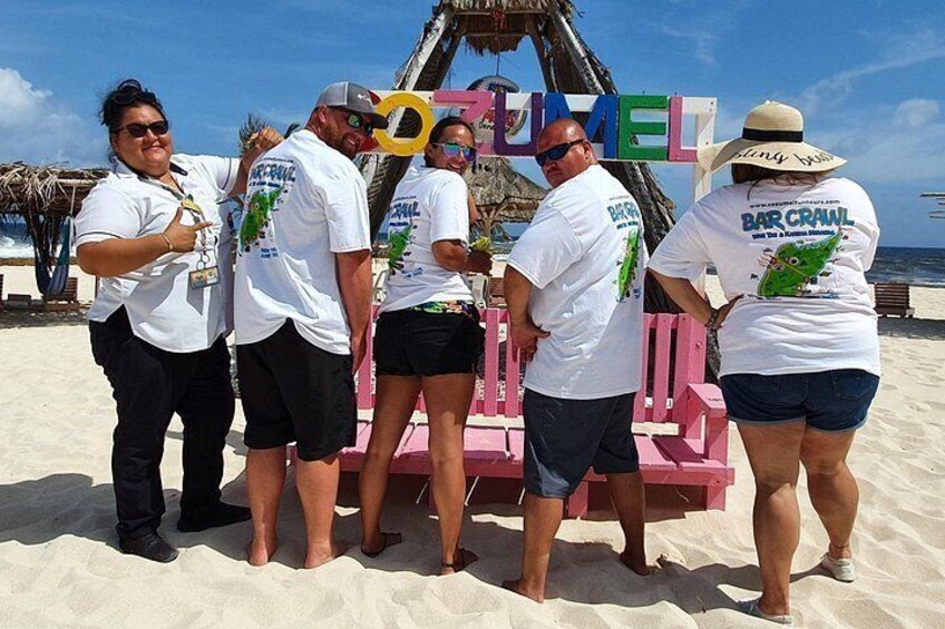 Un grupo de personas de pie en una playa, con un cartel que dice 'BAR CRAWL'. 1