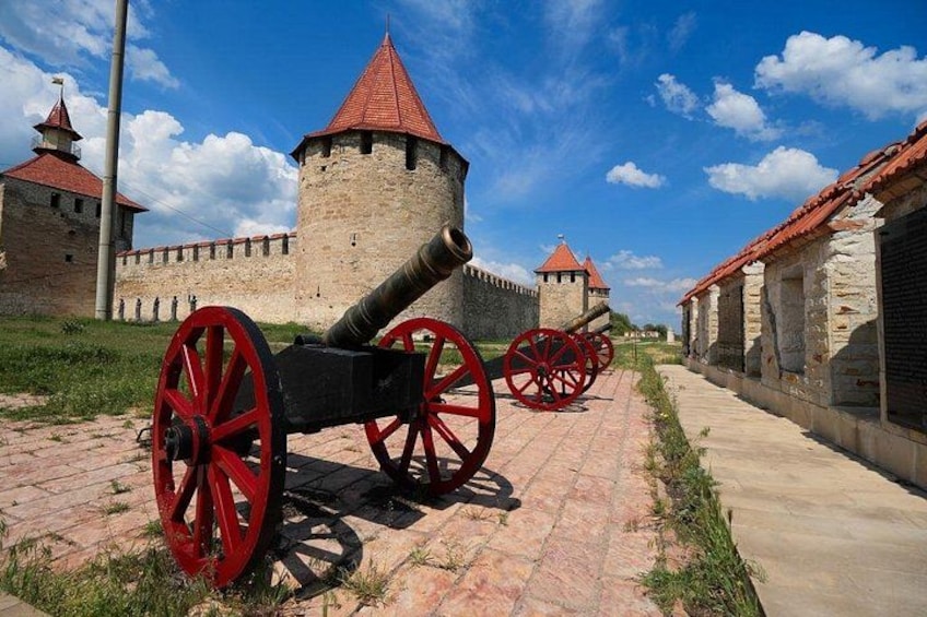 Un cannone storico con ruote rosse, una fortificazione in pietra e un cielo azzurro intenso. 1