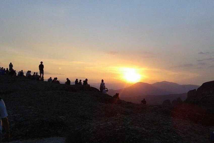 Un coucher de soleil sur un paysage vallonné, avec des personnes assises et debout sur les pentes. 4
