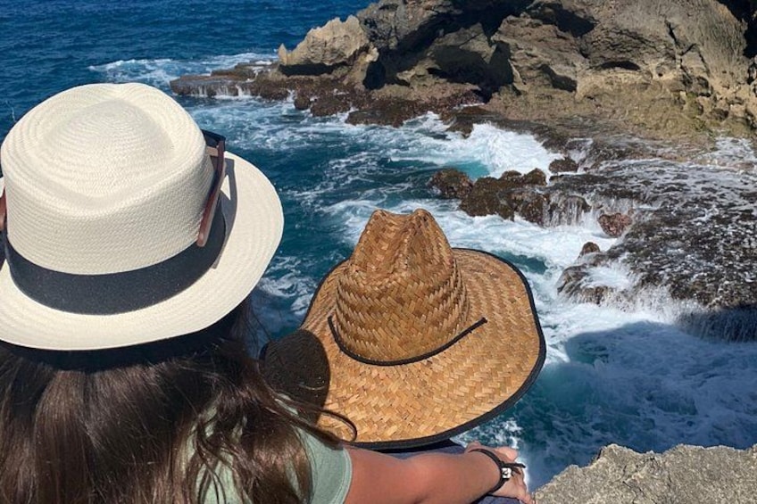 A person wearing a straw hat overlooking a rocky coastline with waves crashing against the rocks. 2