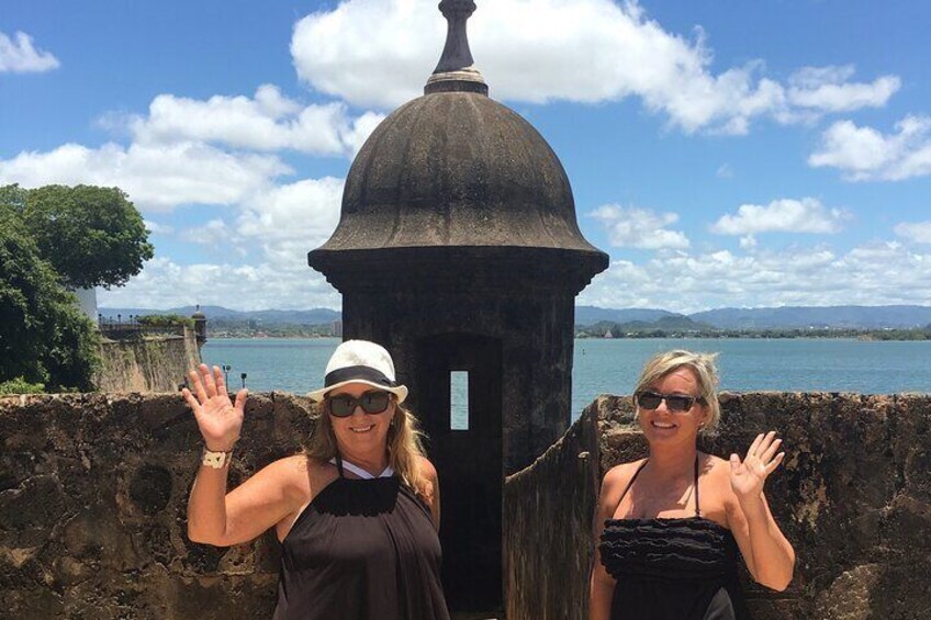 Two people standing in front of a stone structure with a dome, overlooking a body of water and mountains. 4