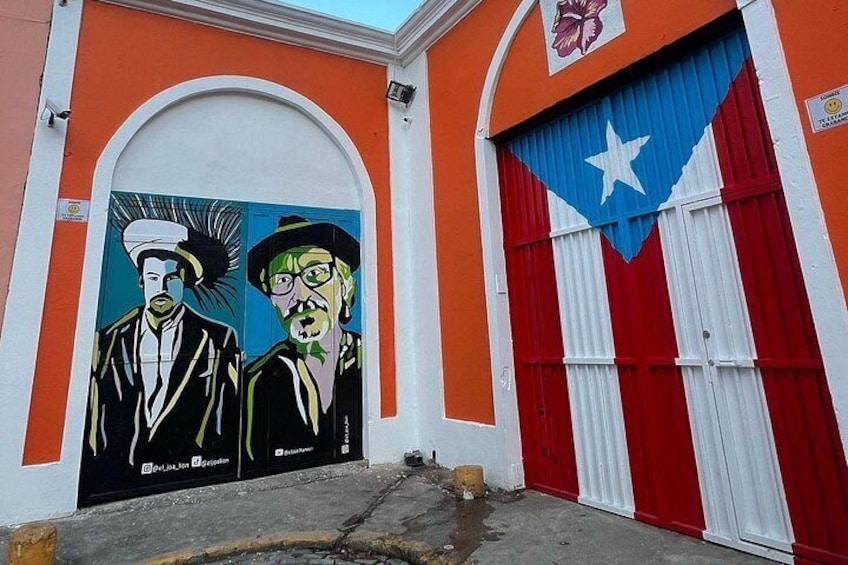A building with a mural of two men, a red and white garage door, and a flag. 4