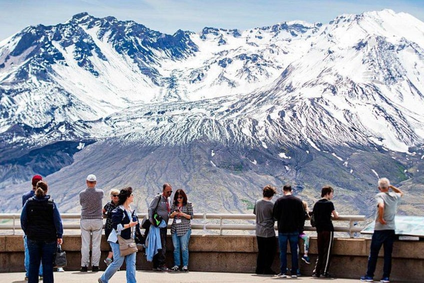 A group of people standing on a viewing platform overlooking a snow-covered mountain range. 4