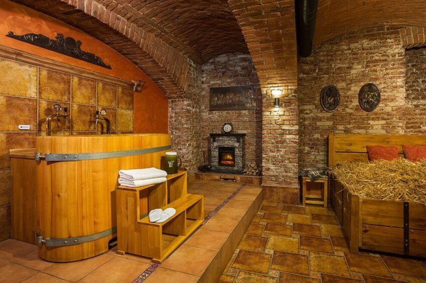 Una habitación rústica con paredes de piedra, una sauna de madera, chimenea y cama con ropa de paja. 2