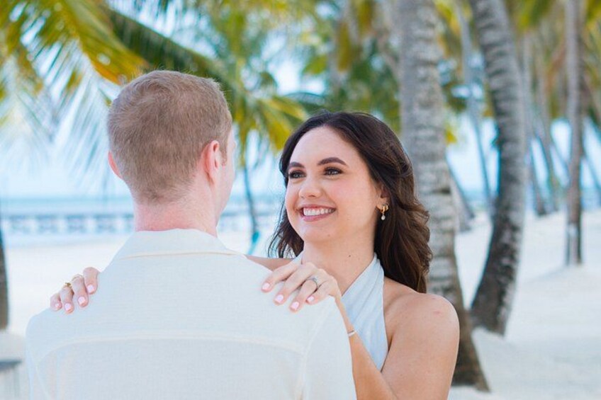 Een koppel omhelst elkaar op een strand met palmbomen en een heldere lucht. 3