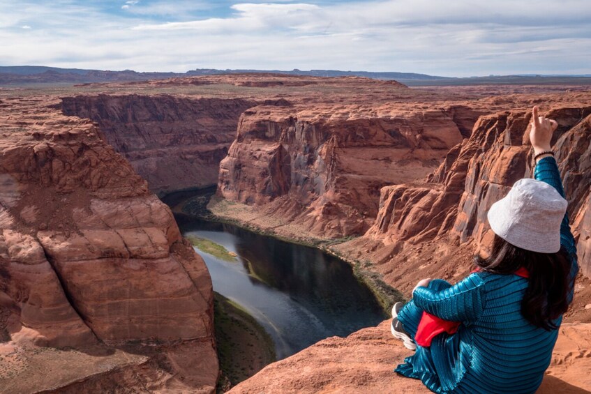 A person sitting on a rock overlooking a canyon with a river. 1