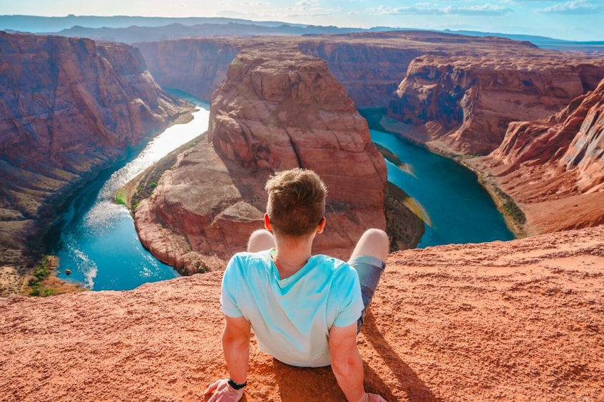 A person sitting on a rock overlooking a canyon with a river. 5
