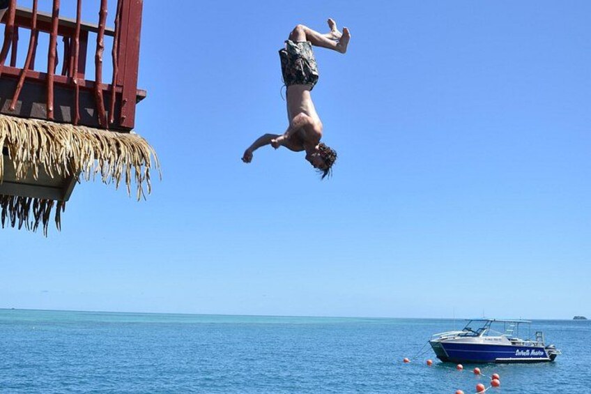 A person diving from a dock into the ocean, a boat, and a clear blue sky. 2