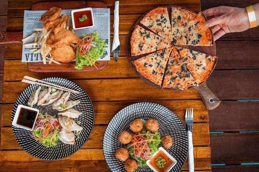 A wooden table with various dishes including fried fish, a pizza, and a plate with meatballs. 4