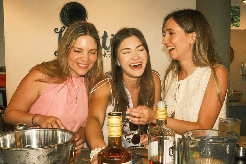 Drie vrouwen aan een tafel met een schaal, flessen en glazen. 4