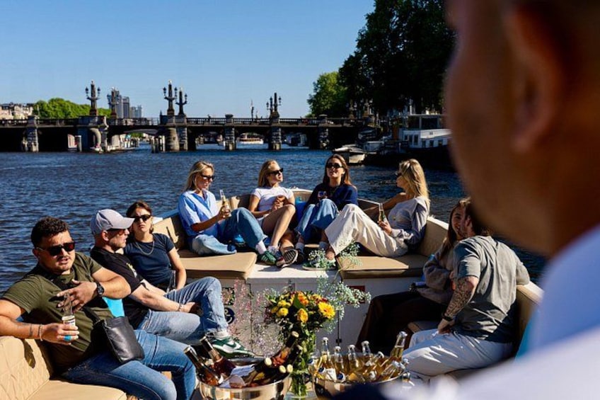 A group of people sitting on a boat by a river with a bridge in the background. 3