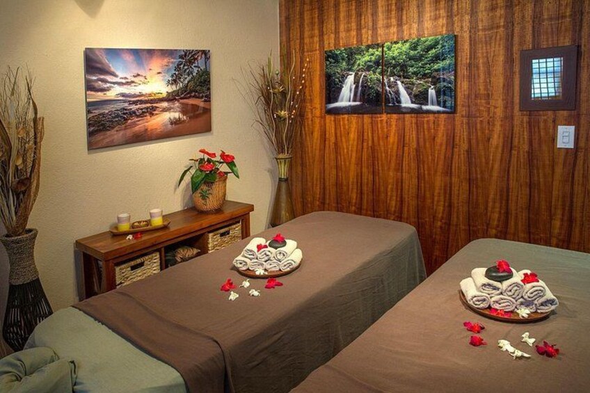 A spa room with two massage tables, a wooden cabinet, and wall-mounted artwork. 3