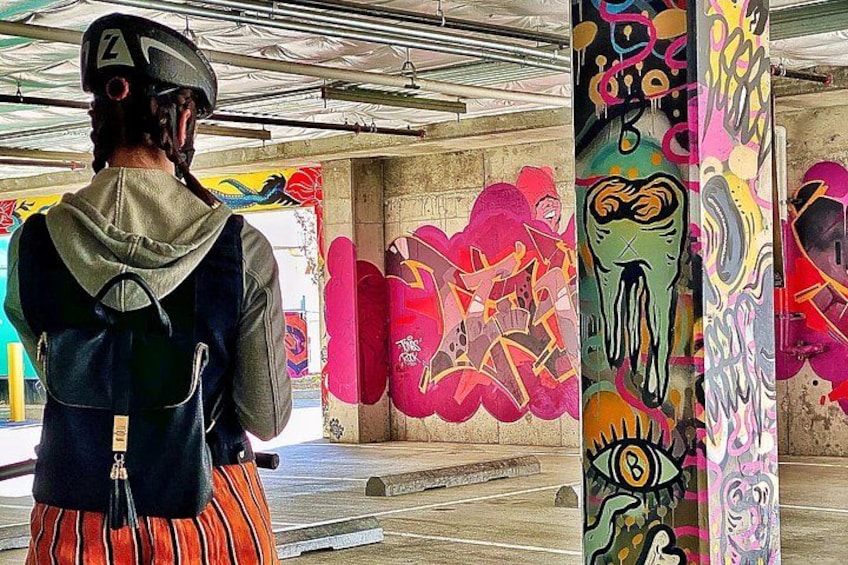 A person wearing a helmet and a backpack, standing in a parking garage with colorful graffiti on the walls. 3