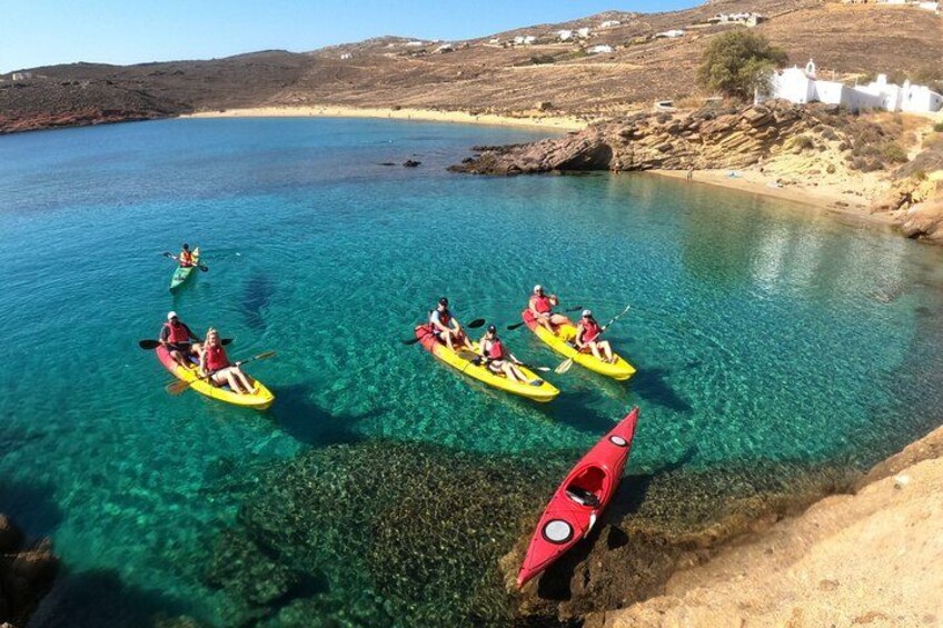 Des personnes pratiquent le kayak sur une mer bleue et limpide, avec une côte rocheuse et des bâtiments blancs en arrière-plan. 2