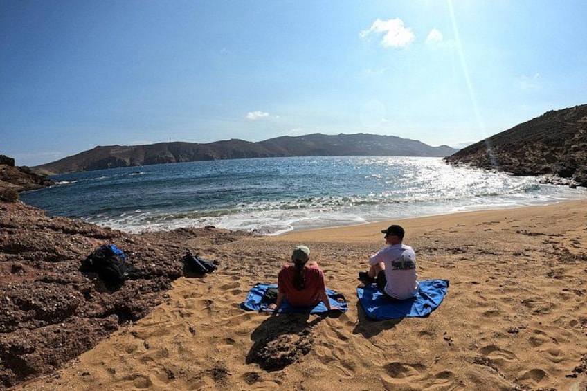 Deux personnes sont assises sur une plage, avec un rivage rocheux et une vue dégagée sur l’océan. 3