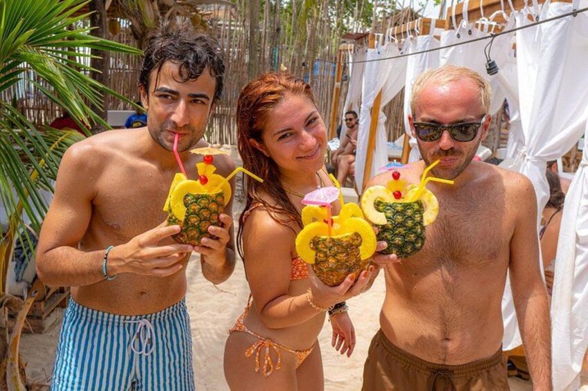 Three people holding drinks with pineapple slices on the beach. 4