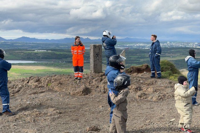 A group of people in outdoor gear, some taking photos, with a mountainous landscape in the background. 1
