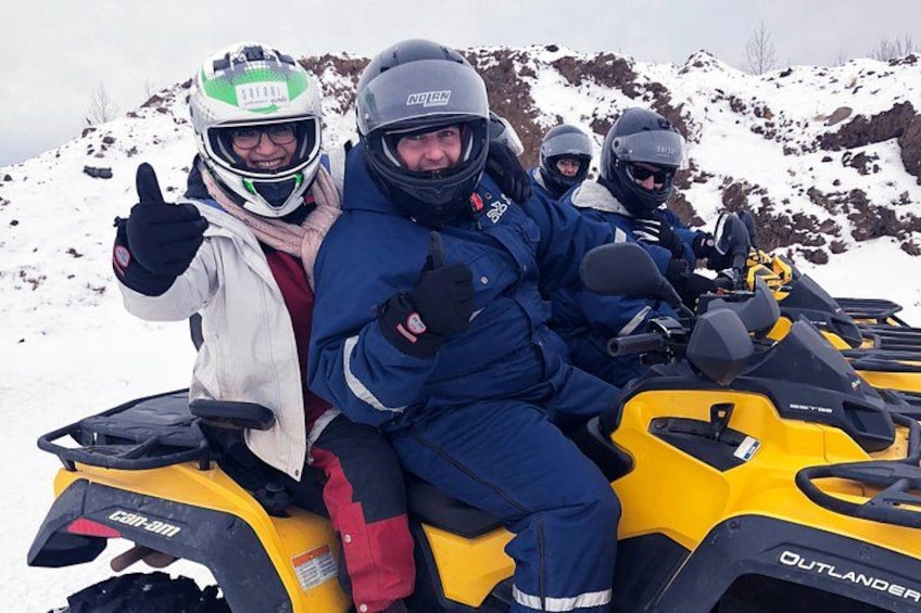 Four people on a yellow snowmobile, wearing winter clothing and helmets, in a snowy mountainous area. 5