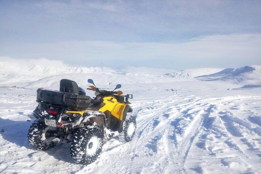 A yellow ATV on a snowy trail with snow-covered mountains in the background. 4