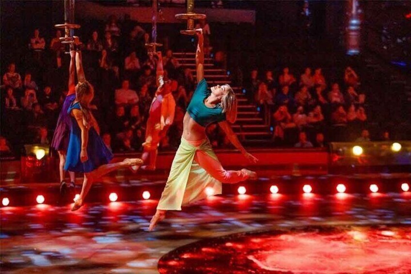 Spettacolo di danza con tre ballerini sul palco, un pubblico seduto e uno sfondo illuminato di rosso. 2