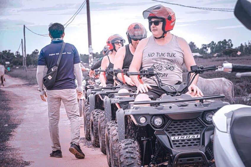 Un gruppo di persone su quad ricreativi su una strada sterrata, con un paesaggio rurale sullo sfondo. 3