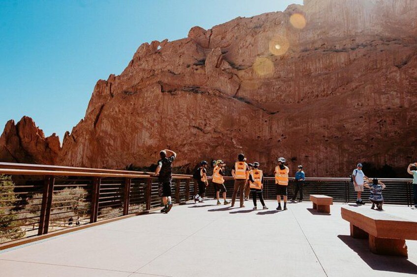 A group of people in orange vests standing on a concrete platform with a large red rock formation in the background. 4