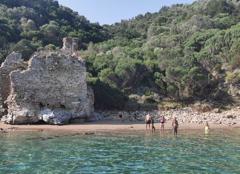 Una spiaggia rocciosa con acque limpide, una rovina in pietra e colline coperte da fitta vegetazione. 4