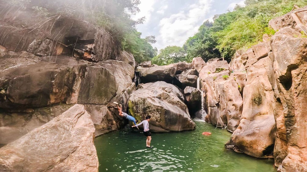 Een rotsachtige canyon met een smalle waterloop en twee mensen die over de rotsen klimmen. 1