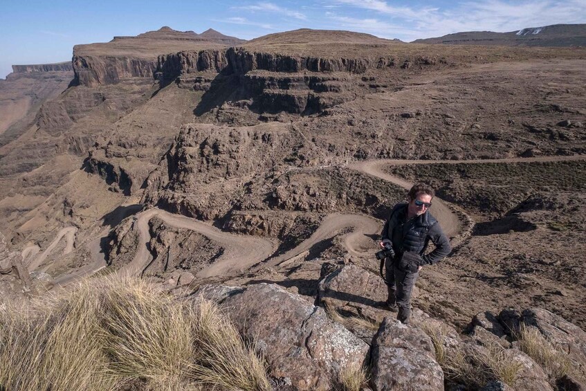 Un terrain accidenté, avec un chemin de terre sinueux, et une personne debout sur un rocher. 4